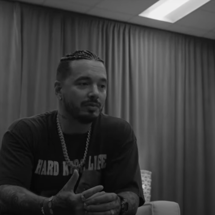 Image of J Balvin sitting in a chair in front of a curtained wall